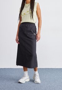 Vaaleanvihreä hihaton toppi, jossa on pyörteinen kuvio, yhdistetty mustaan keskipitkään hameeseen ja valkoisiin urheilukenkiin. Sulavat rakenne ja joustava vyötärö.