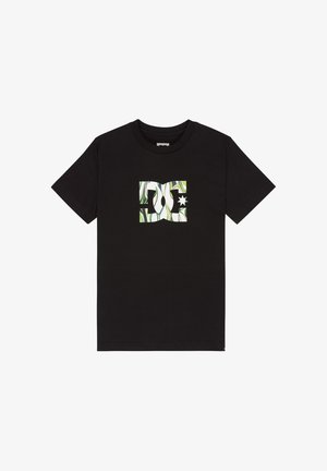 T-shirt noir en coton avec un logo DC vert et blanc, accompagné d'un short en jean bleu clair, de chaussettes blanches et de baskets noires et rouges.