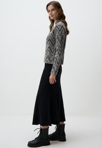 Pull gris à motif en chevrons avec une texture, associé à une jupe maxi noire à côtes et des bottes de combat noires à lacets.
