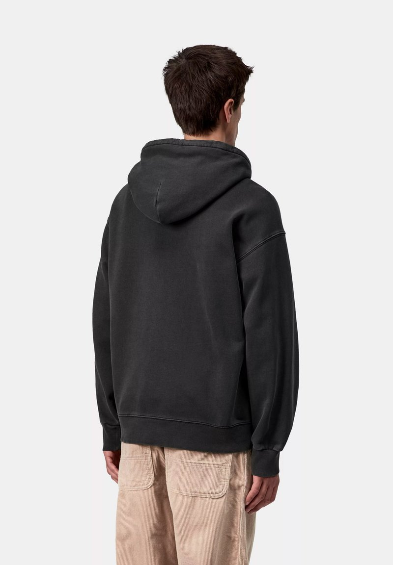 Sudadera gris oscuro con una capucha grande, ajuste holgado y puños acanalados. Textura suave y detalles de diseño mínimos. Combina con pantalones de pana de color claro.