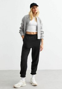 Grijze cardigan, witte crop top, zwarte sweatpants en witte sneakers. Casual outfit met eenvoudig ontwerp en neutrale kleuren.