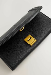 Mustalla nahalla valmistettu clutch-lompakko, jossa on teksturoitu pinta, kultaiset kiinnitysvälineet ja läppä suljenta. Kompakti muotoilu, jossa on minimalistinen estetiikka.