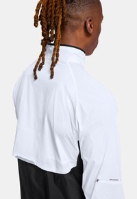 Hvid og sort jakke med cropped design, glat tekstur, høj krave og broderet logo detalje på ærmet.