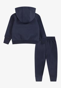 Hanorac albastru marin cu glugă ajustabilă prin șnur și pantaloni jogger asortați. Țesătură moale, manșete și talie ribbed, design simplu fără modele.