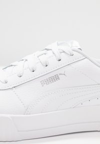 Weiße Ledersneaker mit strukturiertem Obermaterial, flachen Schnürsenkeln, silbernem Puma-Logo und subtilen Designlinien an der Seite und Ferse.