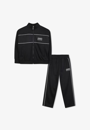 Survêtement noir composé d'une veste zippée avec des rayures blanches et un logo, assortie à un pantalon avec une taille élastique et des rayures latérales.