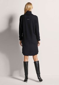 Schwarzes Strickkleid mit hohem Kragen und gerippten Bündchen. Verfügt über ein Logo-Patch auf der Rückseite und einen geraden, knielangen Schnitt.