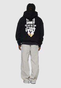 Svart hoodie med vit grafisk text på baksidan som säger "Livet är kort, det är upp till dig att göra det sött," med illustrationer av glasskoner.