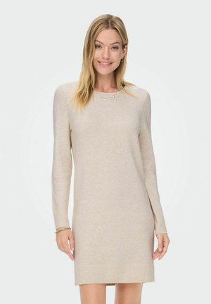 Robe en tricot beige à manches longues avec un ourlet côtelé, un col rond et une texture subtile, agrémentée de petits éléments décoratifs autour du cou.