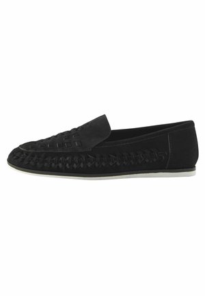 Zapato negro de ante tipo slip-on con detalles trenzados en la puntera y una parte superior suave. La suela es de color claro y tiene un diseño de bajo perfil.
