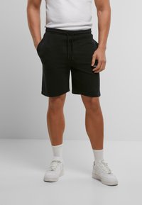 Shorts en coton noirs avec une taille élastique et un cordon de serrage ; poches sur les côtés ; associés à des baskets blanches et des chaussettes blanches de longueur mi-mollet.