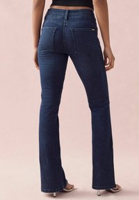 Jeans a zampa di elefante blu scuro con una texture di denim liscia, vita alta e due tasche posteriori, con dettagli di cucitura sottili.
