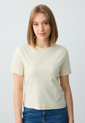 T-shirt beige à manches courtes avec un col rond et une coupe près du corps, fabriqué à partir d'un tissu doux et léger ; associé à un jean bleu.