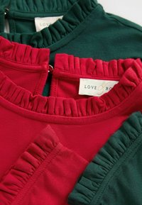 Două bluze din bumbac roșu și verde, având guler cu volane și fermoar la spate; etichete vizibile cu numele brandului "LOVE & ROSE."