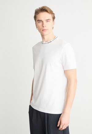 Camiseta de algodón blanca con cuello redondo y un logo negro bordado en el collar. La camiseta tiene mangas cortas y una silueta ajustada.