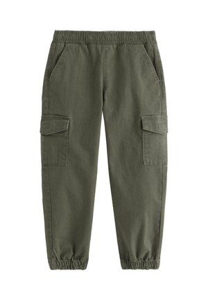 Smilende ung dreng iført en grønstribet langærmet trøje, olivengrønne cargobukser og hvide sneakers, stående med den ene hånd på nakken.