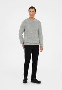 Suéter gris de punto con patrón de trenzas, cuello redondo y puños acanalados, combinado con pantalones negros y botas negras elegantes.