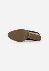 Zapato negro con parte superior de tela texturizada, suela plana y fondo de goma marrón suave. Presenta un sutil logo de TOMS en la suela.
