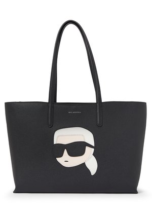 Schwarze Leder-Shopper-Tasche mit langen Griffen, auf der Vorderseite ein stilisiertes Gesicht mit weißen Haaren und schwarzen Sonnenbrillen.