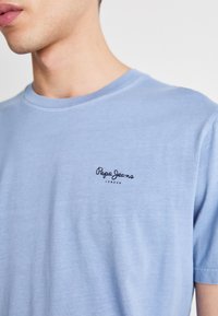 Šviesiai mėlynas medvilninis marškinėlis su apvalia iškirpte, ant kairiojo krūtinės siuvinėtų mažas juodas "Pepe Jeans London" logotipas.