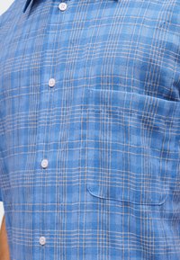 Μπλε κοντομάνικο πουκάμισο με κουμπιά, σε φωτεινό και σκούρο καρό μοτίβο και τσέπη στο στήθος.