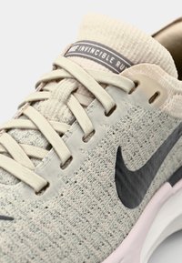 Cremefarbener Nike Sneaker mit einem Mesh-Obermaterial mit strukturierter Oberfläche, schwarzem Swoosh-Logo und einer gepolsterten weißen Sohle. Akzente in beiger Hardware.