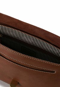 Braune Ledertasche mit strukturierter Oberfläche, ausgestattet mit einem gestreiften Stofffutter und einer Reißverschlusstasche im Inneren, akzentuiert durch helle Nähte.