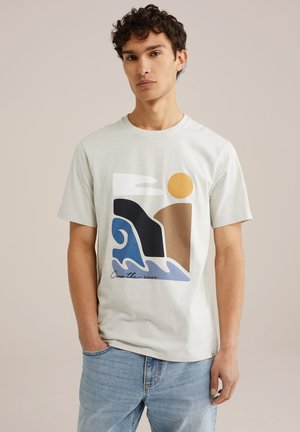 Lichtgrijs katoen t-shirt met een graphic van gebogen golfvormen in blauw en bruin, samen met een gele zon en de tekst "Steek de rivier over."