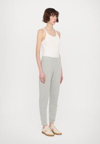 Grijze sweatpants met een elastische tailleband en boorden, gecombineerd met een witte tanktop en beige sneakers met lichte accenten.