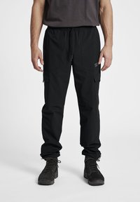 Zwarte cargobroek met een elastische tailleband, meerdere zijzakken, een ontspannen pasvorm en boorden met ritsen voor verstelbare breedte.