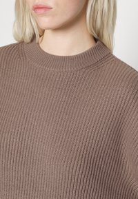 Maglione marrone a coste con scollo rotondo e tessuto testurizzato, dal taglio leggermente oversize e un aspetto morbido e intrecciato.