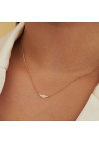 Gouden ketting met een bladerenvormige hanger met uitsnijdingen. Eenvoudig ontwerp, gladde textuur en delicate uitstraling.