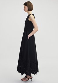 Schwarzes ärmelloses Kleid mit tailliertem Oberteil und fließendem Rock, das am Saum und mit seitlichen Taschen ein detailliertes Augenmuster aufweist.