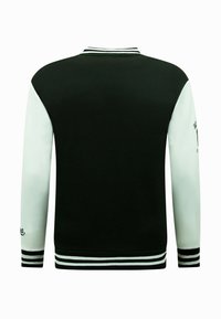 Zwart-witte jas met een geribde kraag, gestreepte manchetten en een geborduurd logo op de mouw. Soepele textuur en sportief ontwerp.