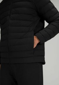 Schwarze Steppjacke mit horizontalem Quiltdesign, Frontreißverschluss und Seitentaschen. Weicher Stoff mit figurbetontem Schnitt.