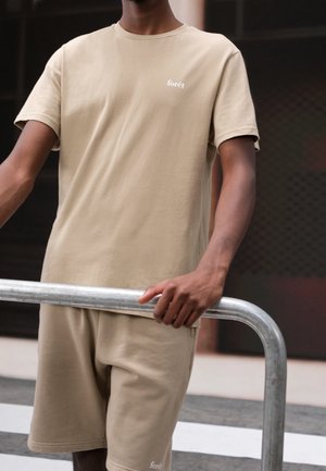 Beige bomulds t-shirt og shorts sæt, med rund hals og korte ærmer. Lille hvid "forêt" logo på brystet. Glat tekstur.