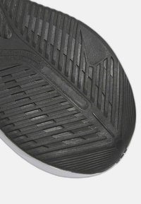 Suela de zapato de goma negra con un diseño texturizado y angular; ranuras y patrones prominentes para tracción; detalles en blanco en el borde delantero.