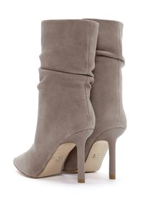 Botas de tobillo de ante gris con un diseño holgado, punta afilada y tacón de 10 cm. Presentan un tacón texturizado y un sutil detalle de marca.