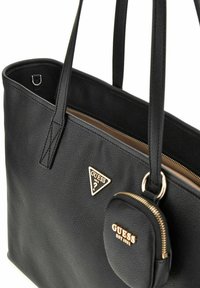 Zwarte leren tote bag met dubbele handvatten, gouden hardware, een driehoekig logo-lapje en een afneembare ritssluitingzak. De binnenzijde is bruin.