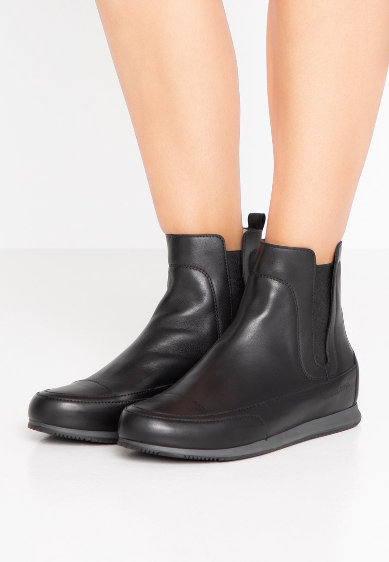 Černé kožené kotníkové boty s elastickými bočními panely, zaoblenou špičkou, hladkou strukturou a minimálním šitím. Gumová podrážka s protiskluzovým vzorem.