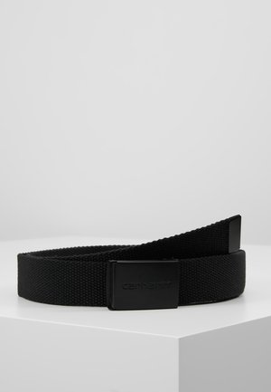 Ceinture en tissu noir tissé avec une boucle rectangulaire noire mate embossée d’un nom de marque, présentée enroulée sur une surface blanche.