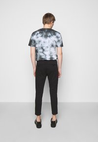 T-shirt noir tie-dye avec des motifs en forme de nuage, accompagnée de pantalons noirs slim-fit et de chaussures noires, vue de dos contre un fond uni.