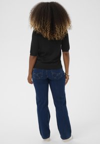 Fekete, rövid ujjú felső, kék harangszárú farmerrel párosítva, elhalványult részletekkel és kidolgozott hátsó zsebekkel, semleges háttér előtt.