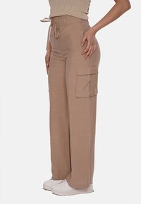 Pantaloni cargo beige con vita elastica e gambe larghe, dotati di tasche laterali e una texture liscia, abbinati a sneakers bianche.