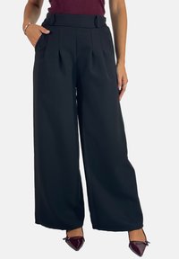 Brede zwarte broek met plooien aan de voorkant, een hoge taille en zijzakken. Glad materiaal en een getailleerde pasvorm zijn duidelijk zichtbaar.