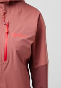 Giacca leggera e resistente all'acqua in una gradazione di rosa e bordeaux. Caratterizzata da cappuccio regolabile, cerniere rosse e logo sul petto.