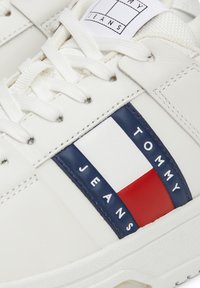 Sneaker in pelle bianca con dettagli blu, rossi e bianchi. Presenta lacci, un marchio sul lato e una suola in gomma testurizzata.