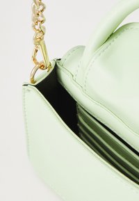 Green leather handbag with a structured shape, featuring a gold chain handle and black inner lining with card slots.