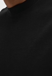 Černé tričko s kulatým výstřihem vyrobené z hladkého, měkkého materiálu. Má minimalistický design bez viditelných vzorů nebo log.
