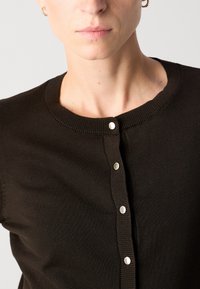 Čierny pletený cardigan s okrúhlym výstrihom, ktorý má strieborné gombíkové akcenty na prednej strane a textúrované rebrované okraje.